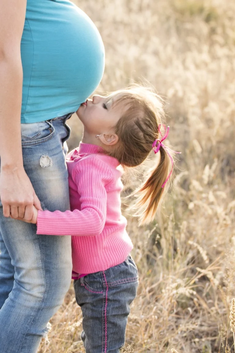 A child kissing a pregnant woman's belly.