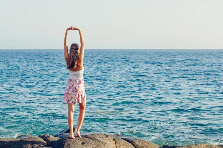 A woman stretching and gazing at the sea.